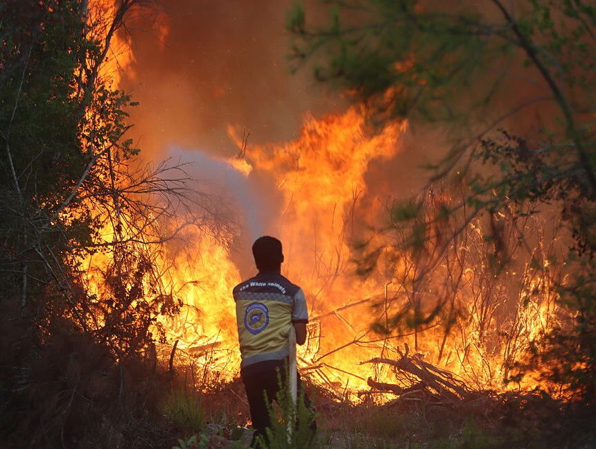 Image of a lone person with a hose, standing before a wall of flame.