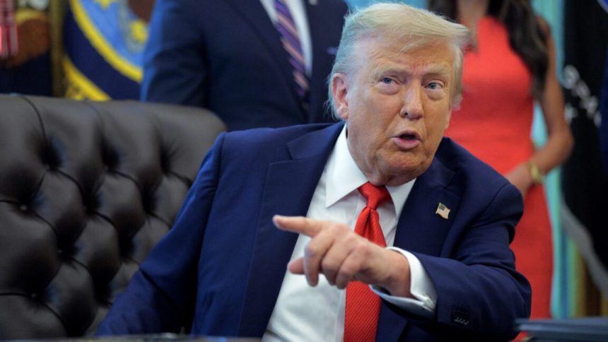 President Donald Trump sits at his desk and talks while pointing a finger.