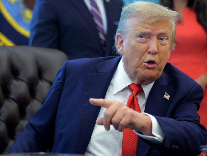 President Donald Trump sits at his desk and talks while pointing a finger.