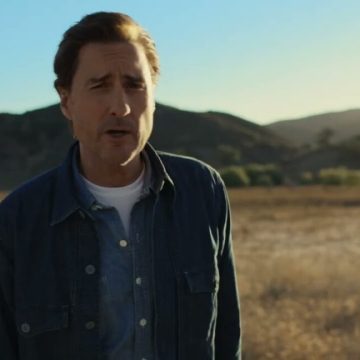 Luke Wilson stands outdoors in a rural area while talking during a commercial for AT&T
