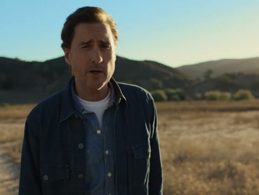 Luke Wilson stands outdoors in a rural area while talking during a commercial for AT&T
