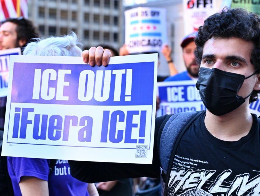 A protestor holds a sign that says "ICE OUT!"