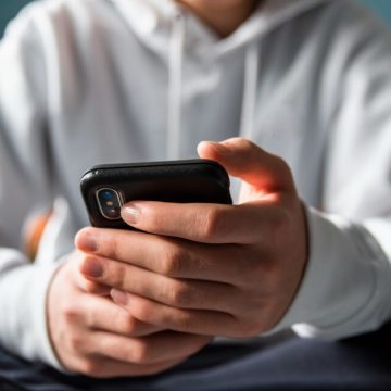 Closeup of the hands of a teen boy texting on a phone.