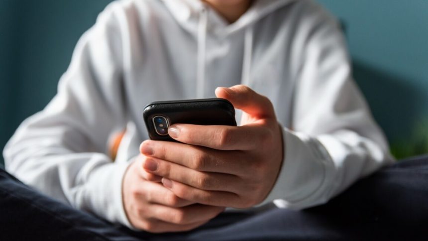 Closeup of the hands of a teen boy texting on a phone.