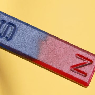 A yellow background with a bar magnet in the foreground, with the magnetic north painted red, and the magnetic south pained blue.