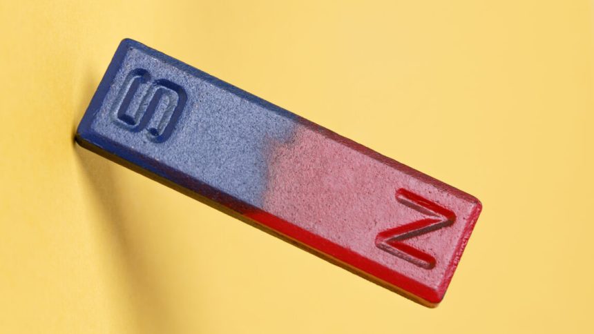 A yellow background with a bar magnet in the foreground, with the magnetic north painted red, and the magnetic south pained blue.