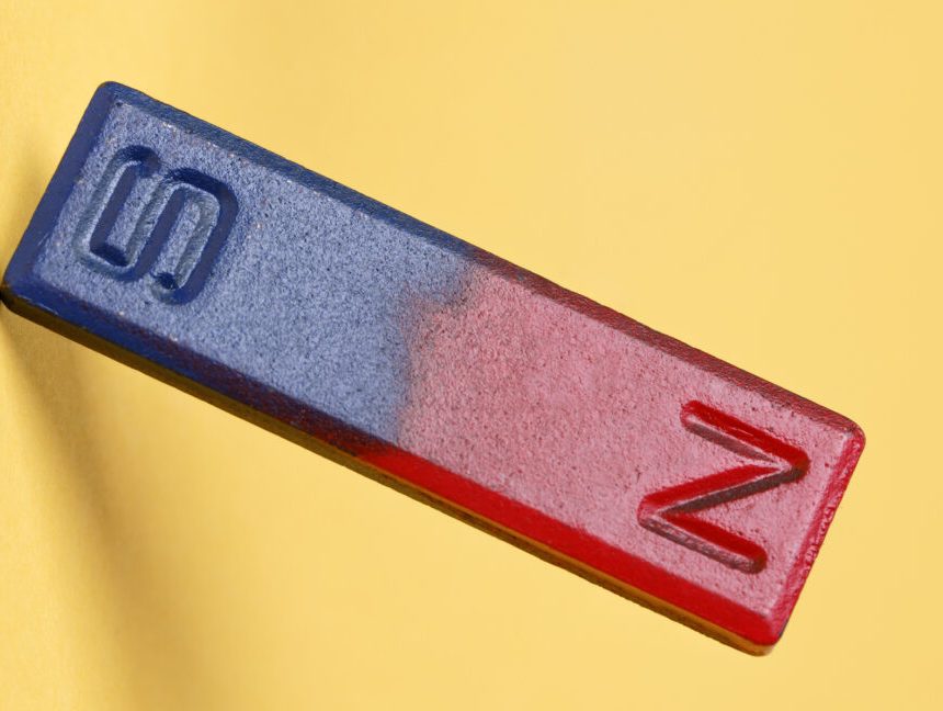 A yellow background with a bar magnet in the foreground, with the magnetic north painted red, and the magnetic south pained blue.