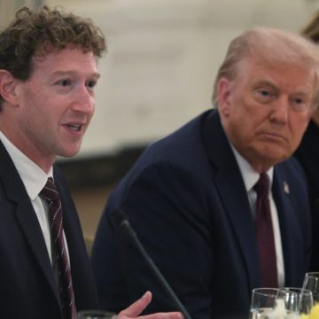 Mark Zuckerberg, Donald Trump, and Melania Trump sit next to each other at a table while Zuckerberg speaks into a microphone.