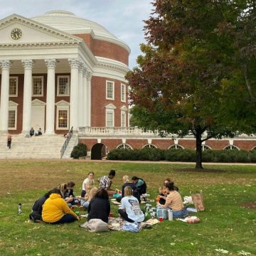 A large lawn dotted with students ends at the steps of a red brick building with a dome and classical colonnade.