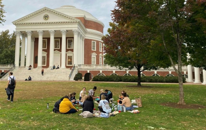 A large lawn dotted with students ends at the steps of a red brick building with a dome and classical colonnade.