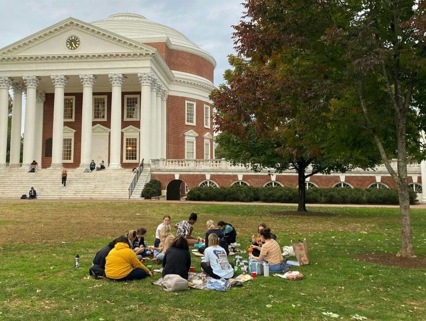 A large lawn dotted with students ends at the steps of a red brick building with a dome and classical colonnade.