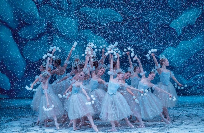 cluster of dancers in ballet costumes dancing for a performance of the nutcracker while snow falls around them