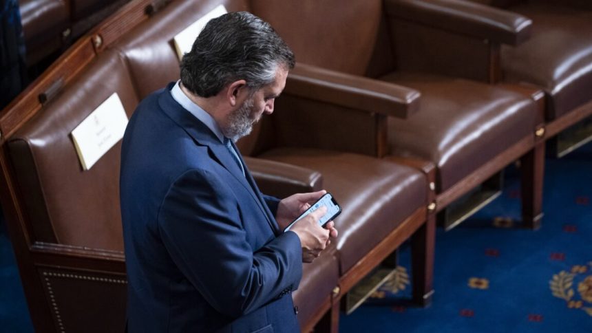 Senator Ted Cruz standing and looking down at his phone.