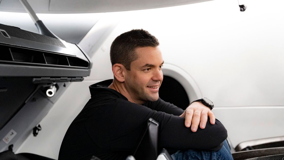 A young man smiles while sitting amidst machinery.
