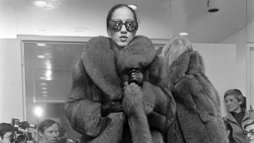 Model Pat Cleveland walks the runway in a fur coat and sunglasses from Halston's fall 1977 ready to wear collection.