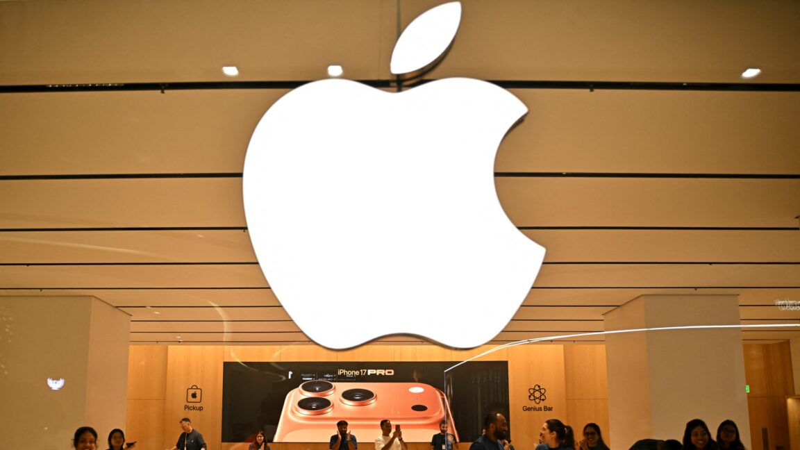 A large Apple logo hangs over employees at an Apple Store in India.