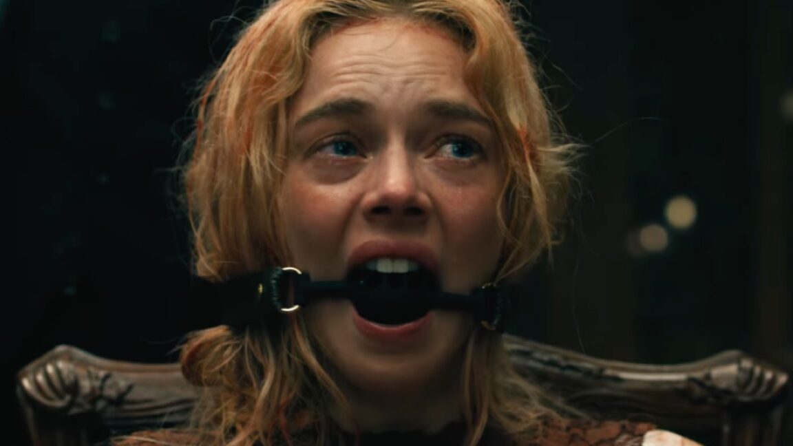 dirty blood spattered blonde woman in a bedraggled wedding dress tied to a chair with a ball gag in her mouth.